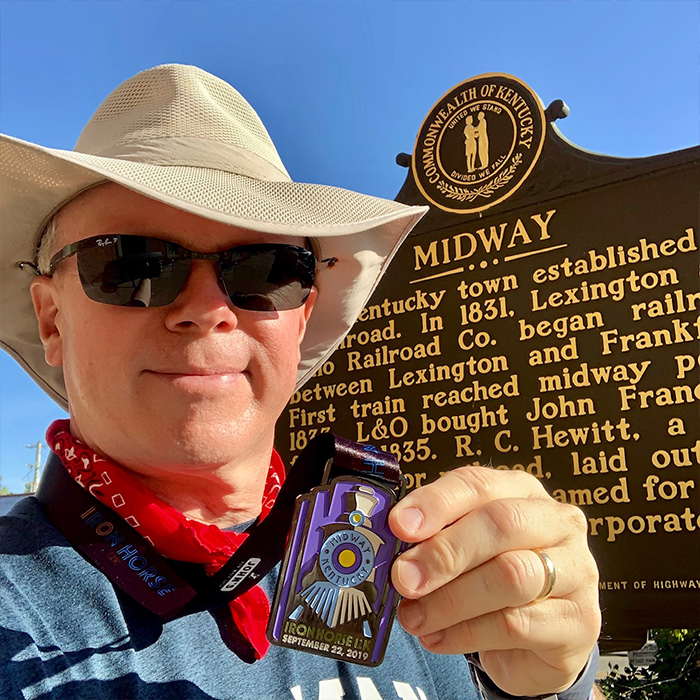 Man with a badge in front of a plaque for Midway